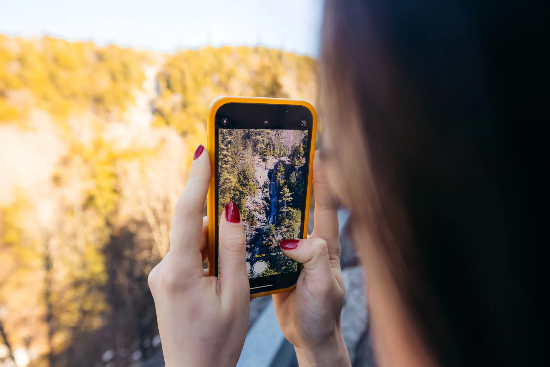 A woman takes a photo of a waterfall. 